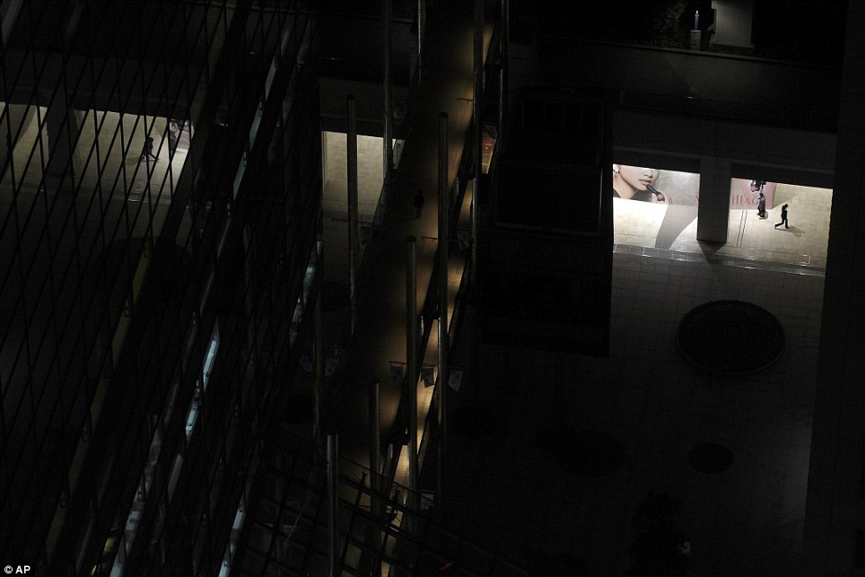 Eerie: People weave their way between blacked out high rises. Tokyo faces at much as six months of blackouts 