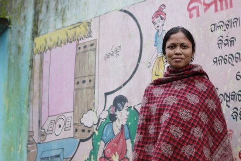 Chandramani Jani in front of a public awareness mural about toilets and sanitation by her home in Chakarliguda.