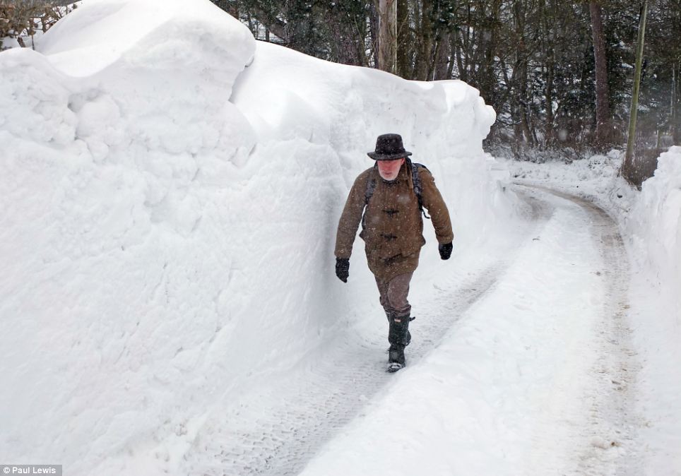 Drifting: A man walks past a packed wall of snow in Dinbren, Denbighshire, caused by snow drifting
